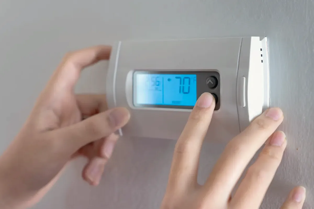 Hands adjusting a digital wall thermostat
